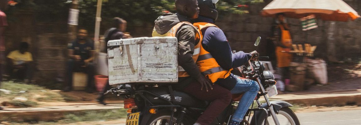 Man in a moving truck holds a box, smiling, with Nairobi cityscape in the background.