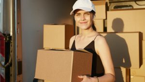 Smiling movers in uniform pose with boxes beside a moving truck.