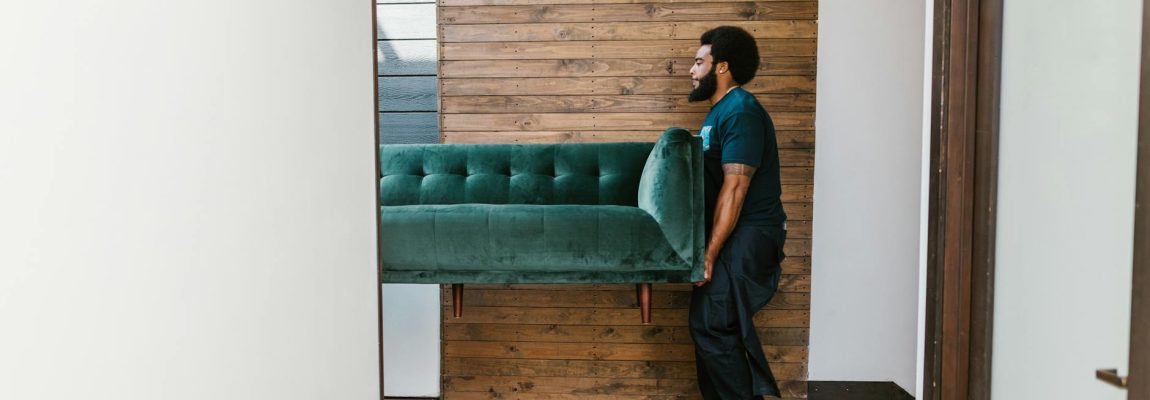 Professional movers carrying a sofa into a moving truck in a residential neighborhood.