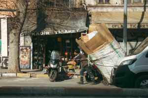 A smiling man in a yellow Top Best Movers shirt loads a large box onto a truck near Mosor.