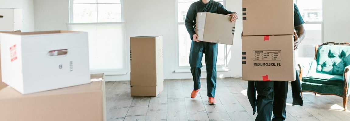 Two smiling movers carry furniture into a moving truck.