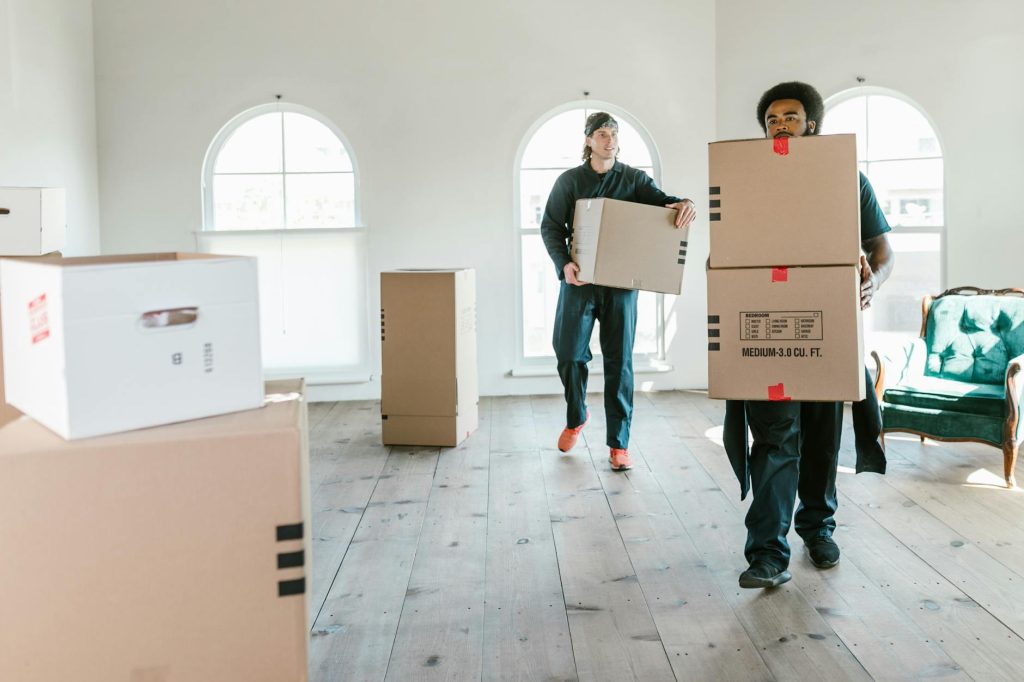 Man in a blue uniform helps a woman and child board a large moving truck with household items.