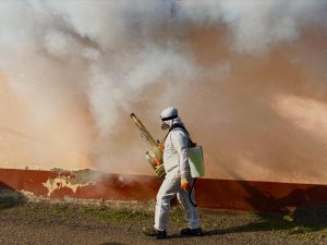 A worker in protective gear sprays pesticide inside a house for fumigation.